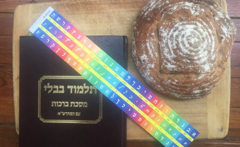 A round loaf of bread and a Talmud sit on a wooden cutting board.