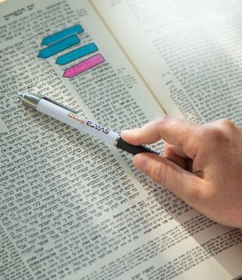 A person points towards a page of Talmud with a pen that reads, "SVARA: A Traditionally Radical Yeshiva."