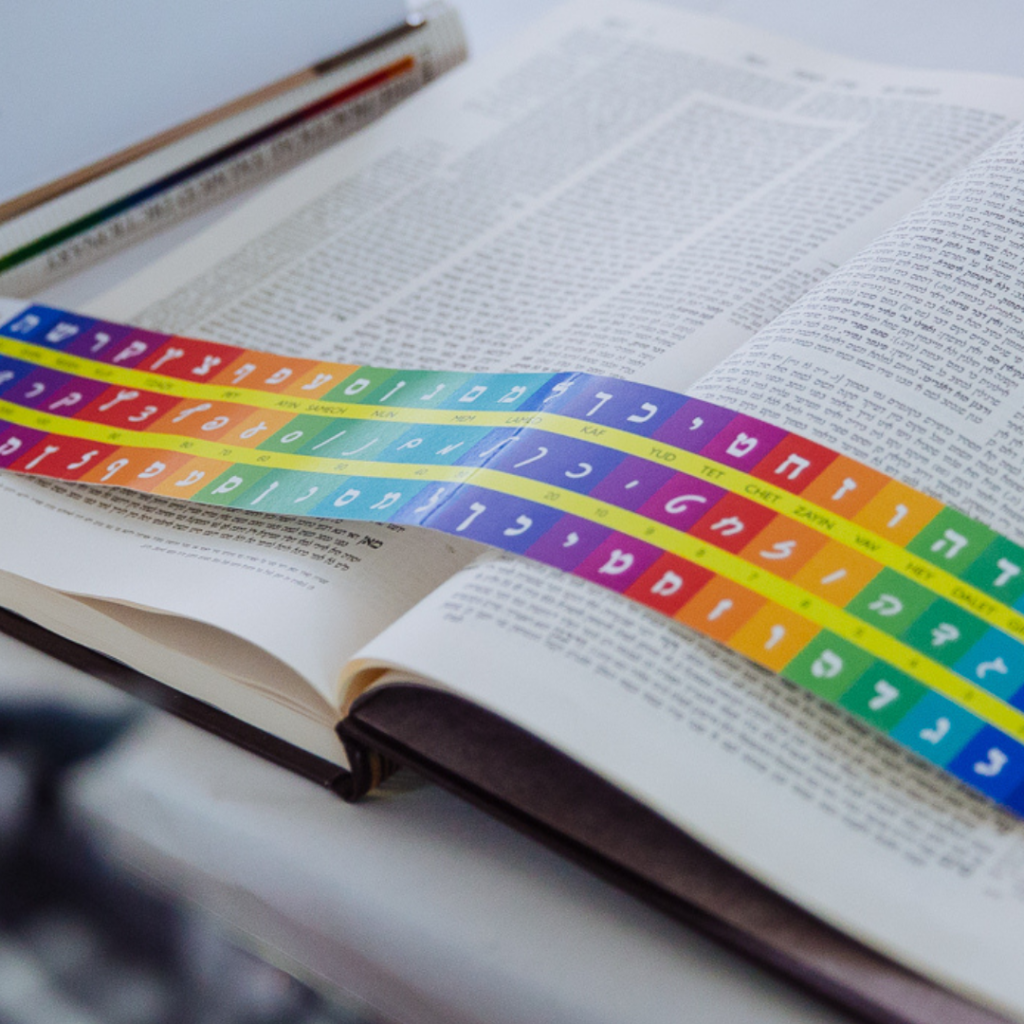 A rainbow alef-bet ruler is resting on a page of Talmud.
