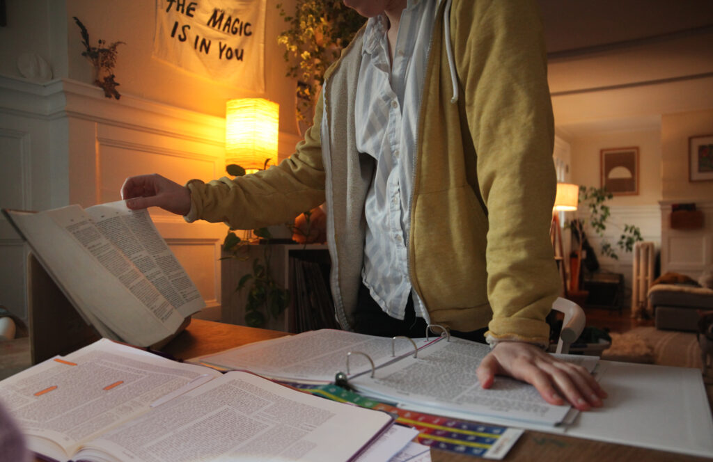 A learner studies Talmud at a large table in their home. Warm lights surround them, and an open masechet can be seen in front of them.