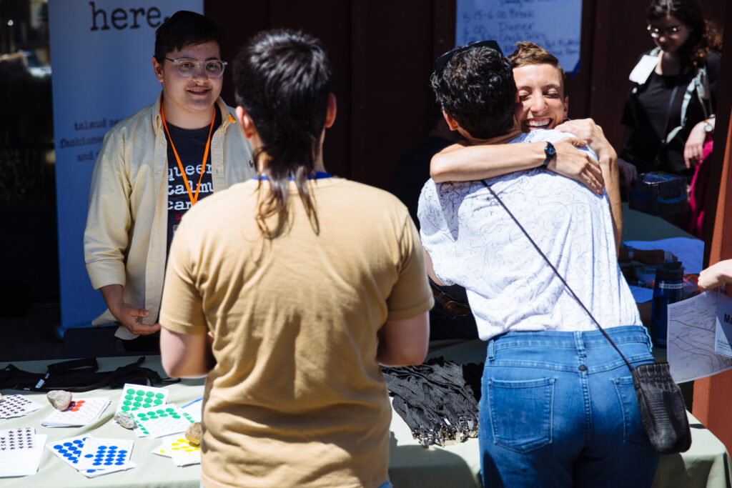 Rabbi Mónica hugs a learner at the registration table for Queer Talmud Camp.